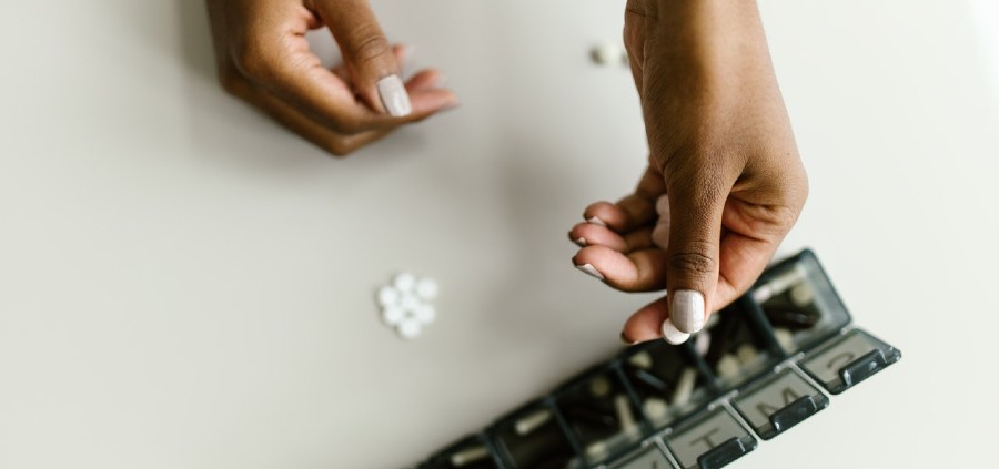 Woman's hands taking pills from a black pill box case