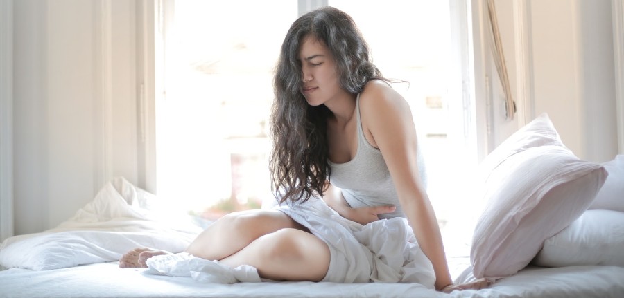 Girl leaned over in bed holding abdomen | Artvigil side effects explained on BuyModa