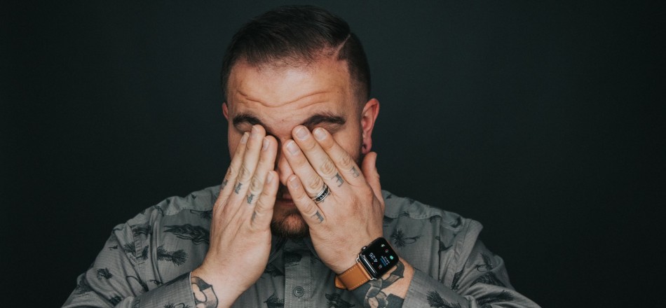 tired tattooed man in grey shirt covering face with hands
